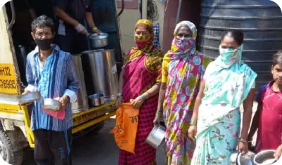 Women standing in line with containers to receive food from a distribution vehicle 